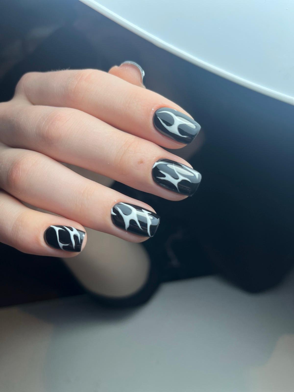 Hand met zwarte nagellak met witte, abstracte vlammen als nagelkunst.