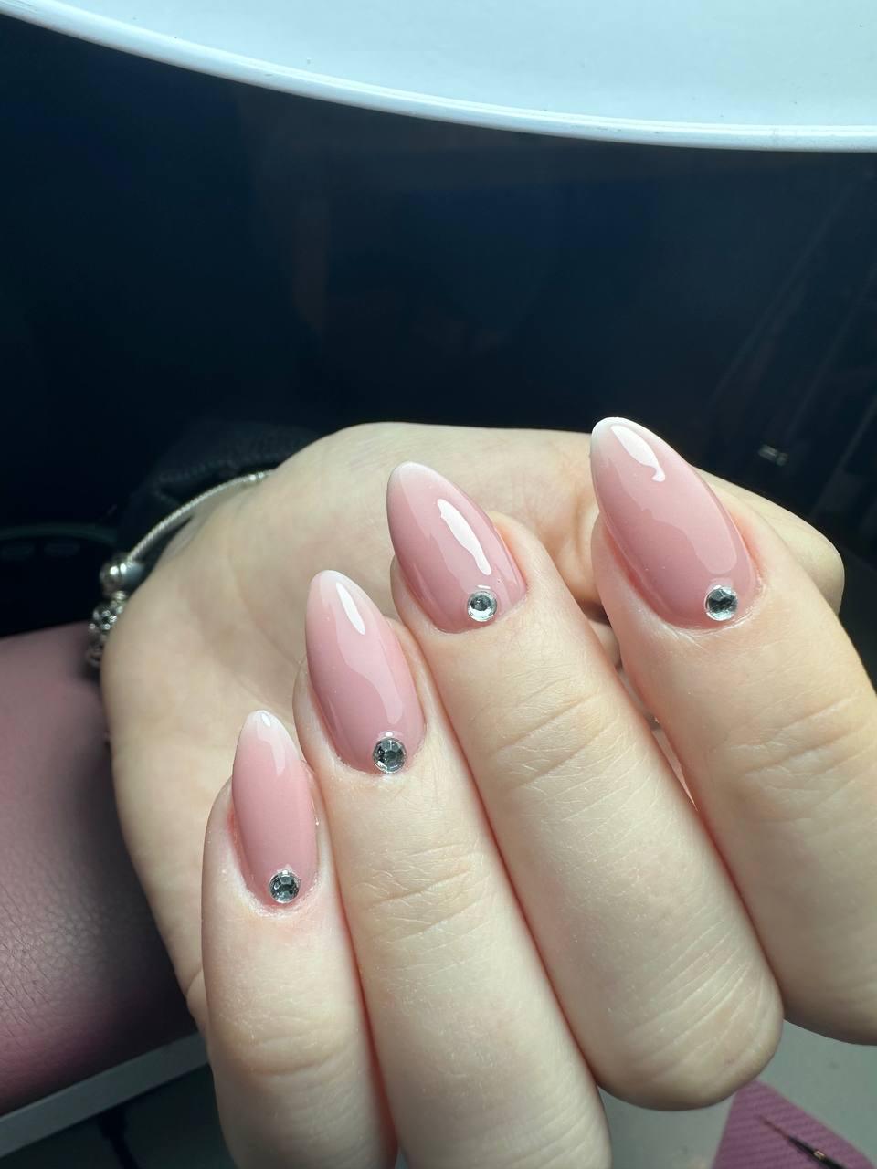 Hand met lange, puntige roze nagels, elk versierd met een kleine zilveren steen bij de nagelriem.