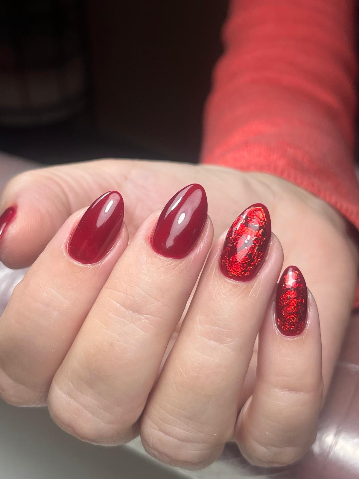 Handen met rood gelakte nagels met ster- en hartmotieven, zittend op een lichte paarse achtergrond en witte gebreide mouwen.