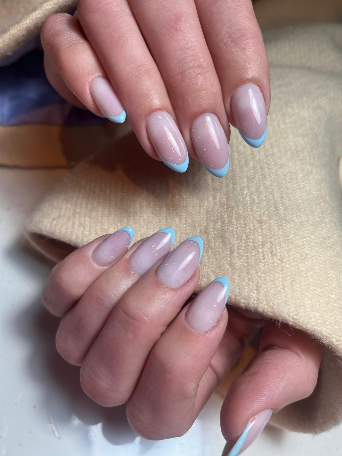 Handen met elegant gelakte, puntige nagels in een subtiele roze tint met lichtblauwe Franse manicure puntjes.