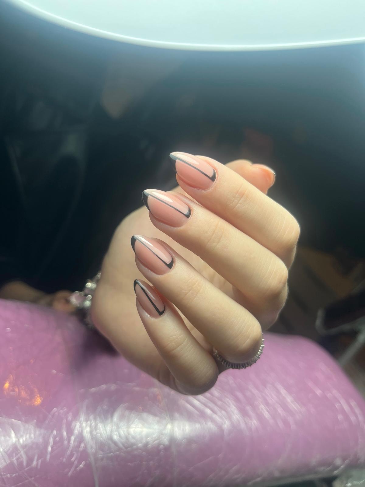 Hand met nagels in lichtroze lak met een slanke zwarte lijn rondom als nagelkunst.