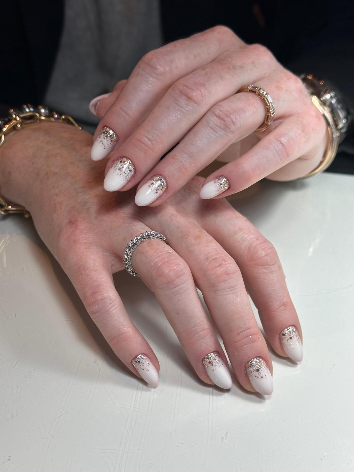 Handen met wit glinsterende ombre nagellak en sieraden, waaronder een gouden ring en een met strass stenen.