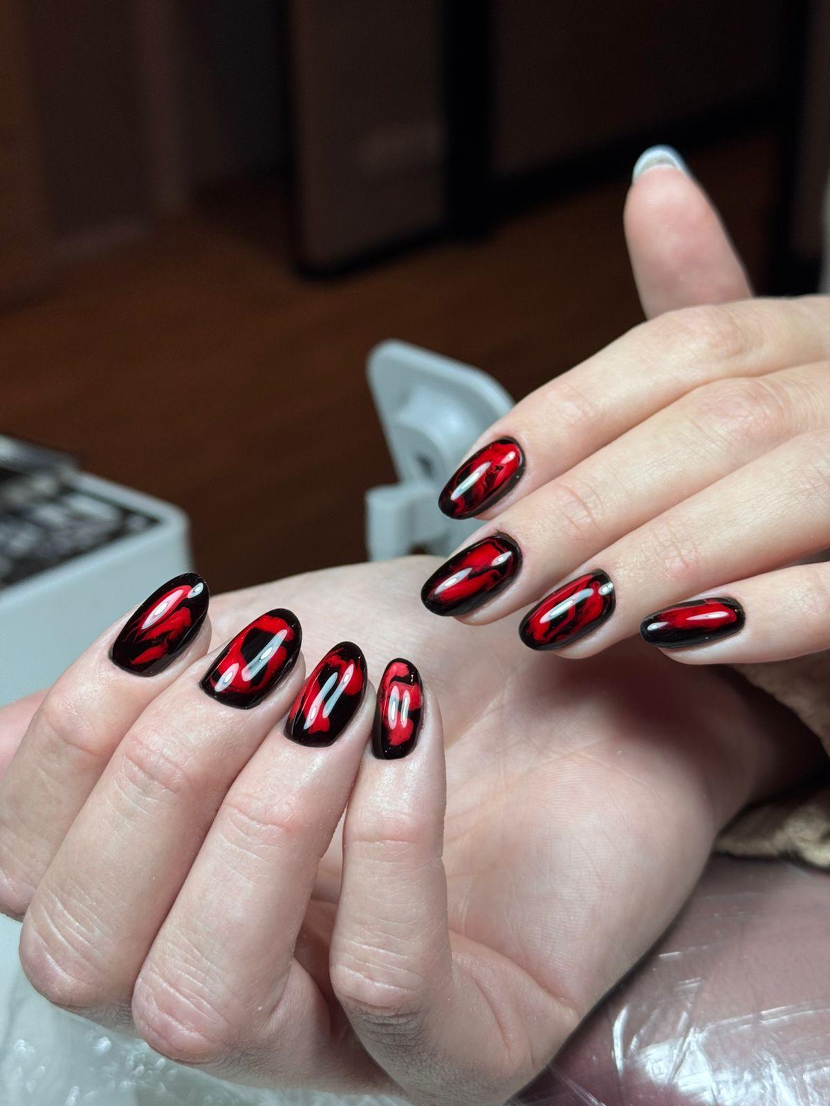 Hand met lange, puntige nagels gelakt in glanzende lila kleur, hand draagt een roze trui.