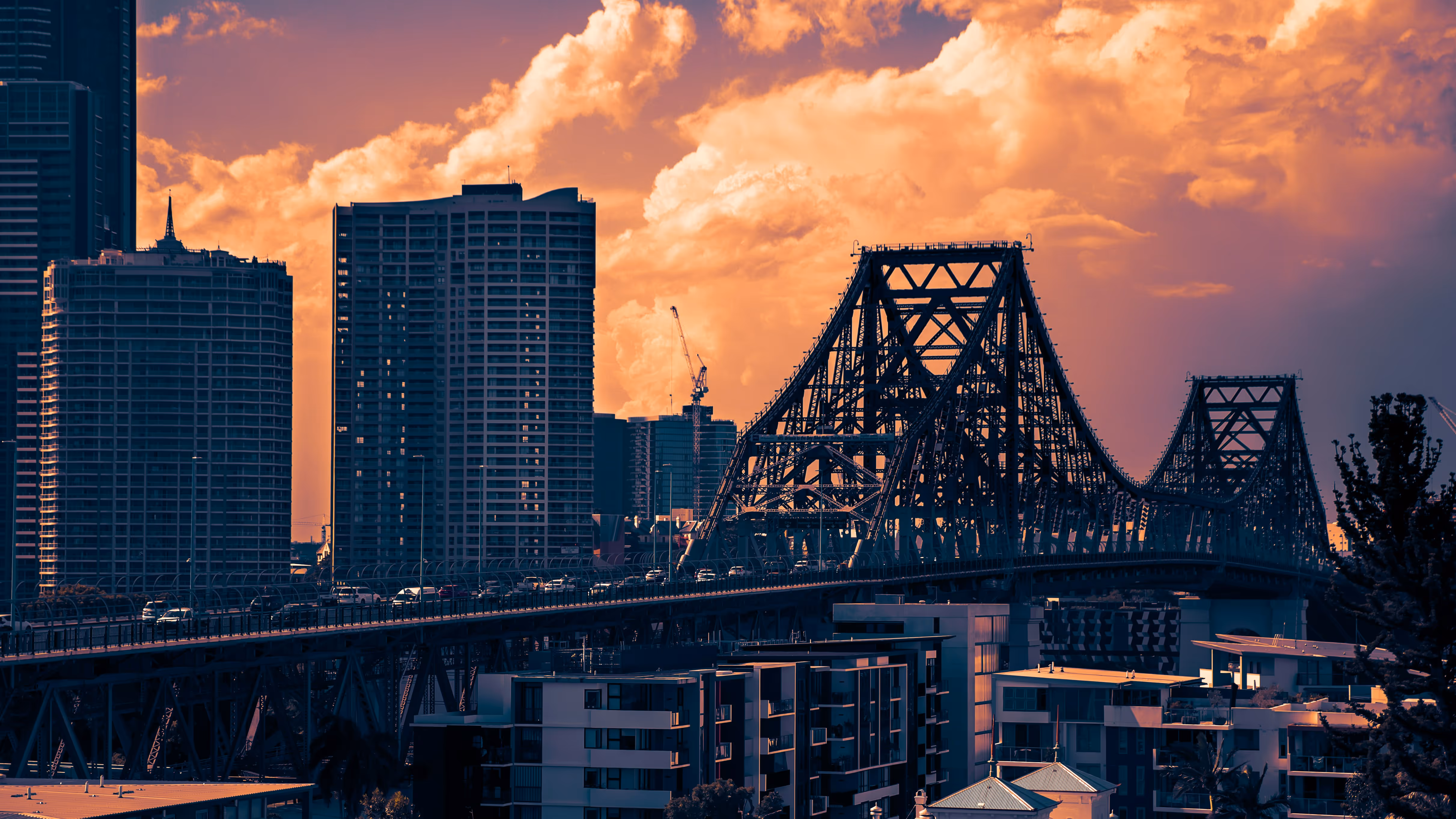 Steel truss Story Bridge in Brisbane at sunset with city buildings and dramatic clouds in the background.
