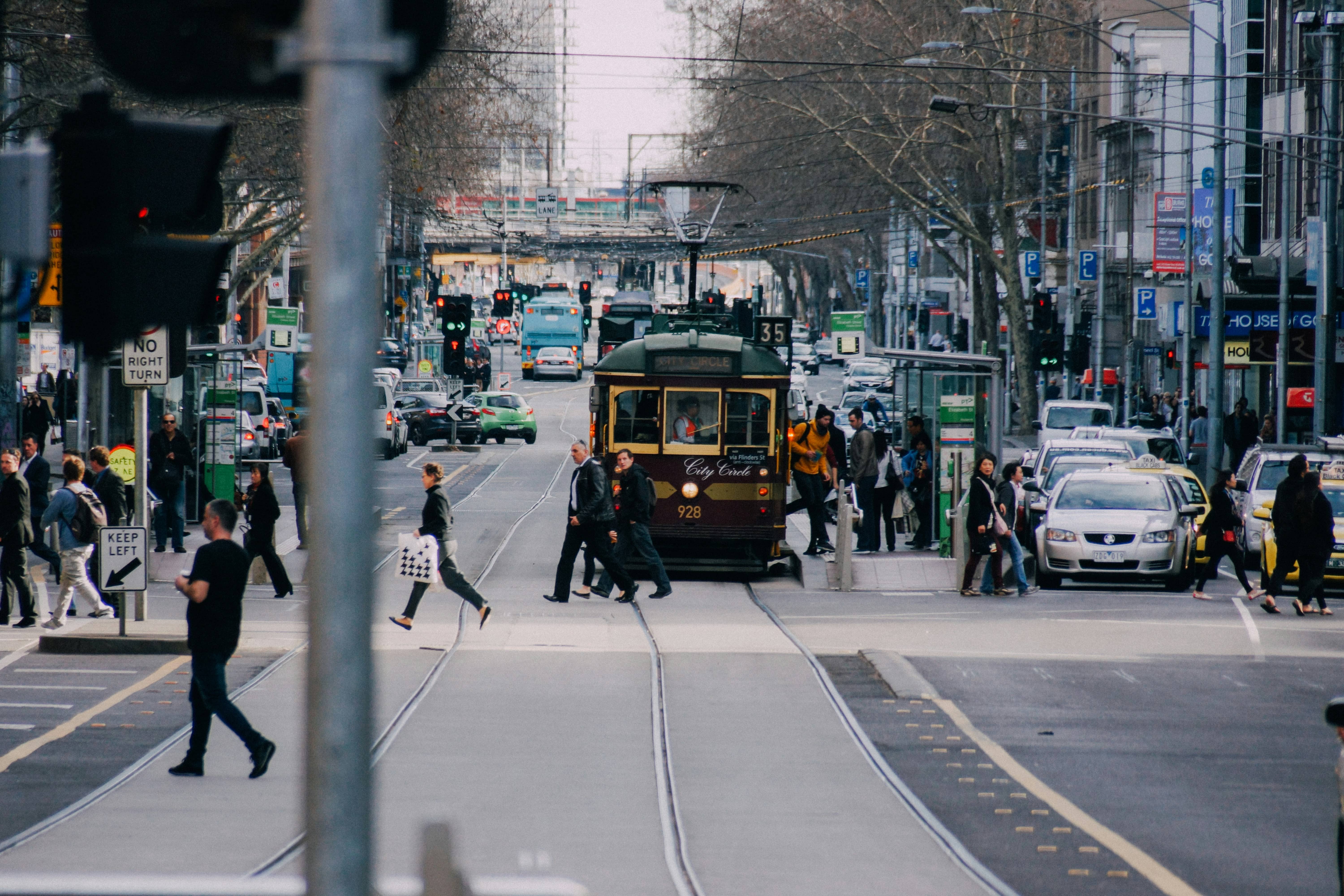 A Melbourne City Circle tram on tracks with pedestrians crossing and cars on a busy city street.
