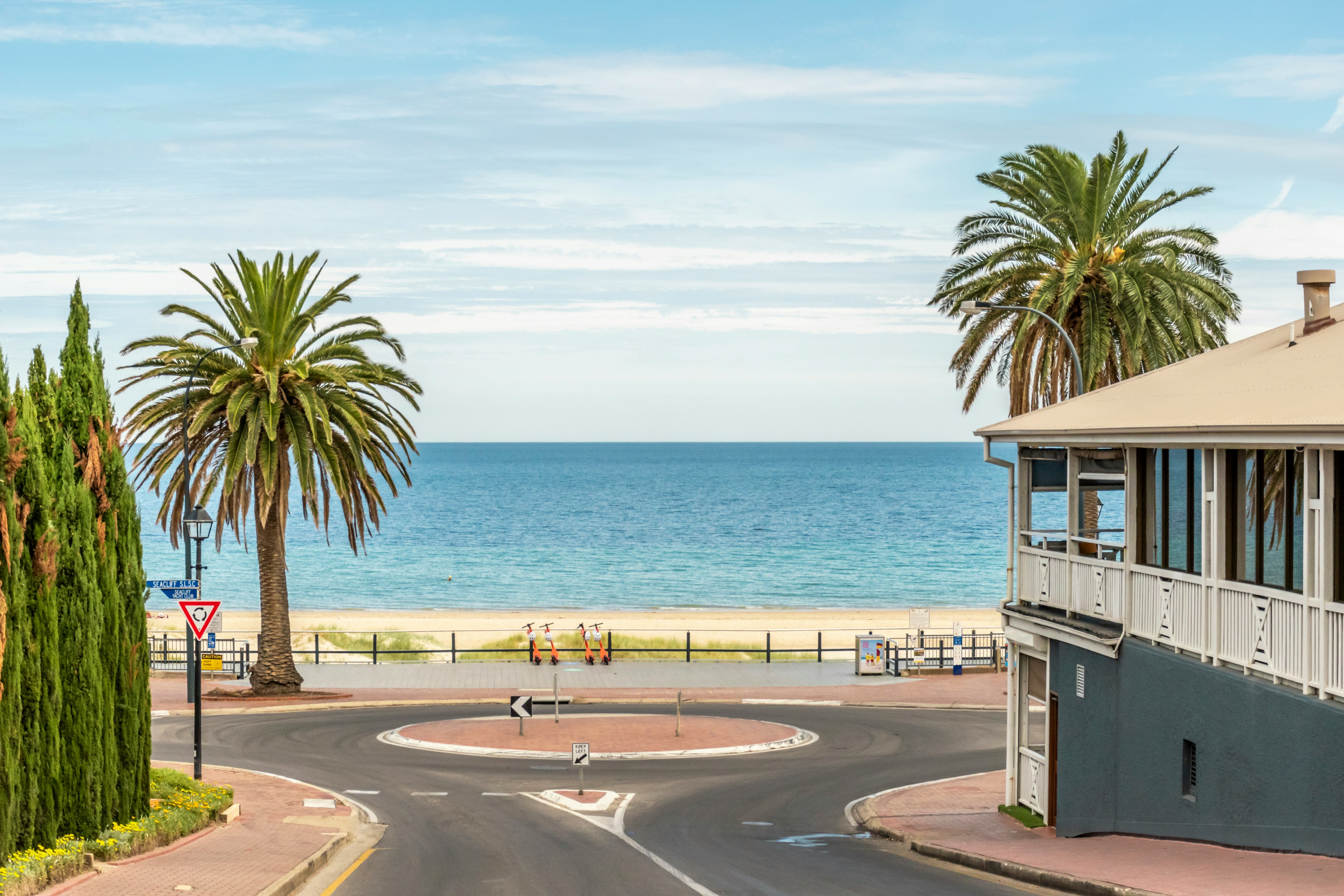 Beachfront roundabout with palm trees and clear blue ocean under a partly cloudy sky.