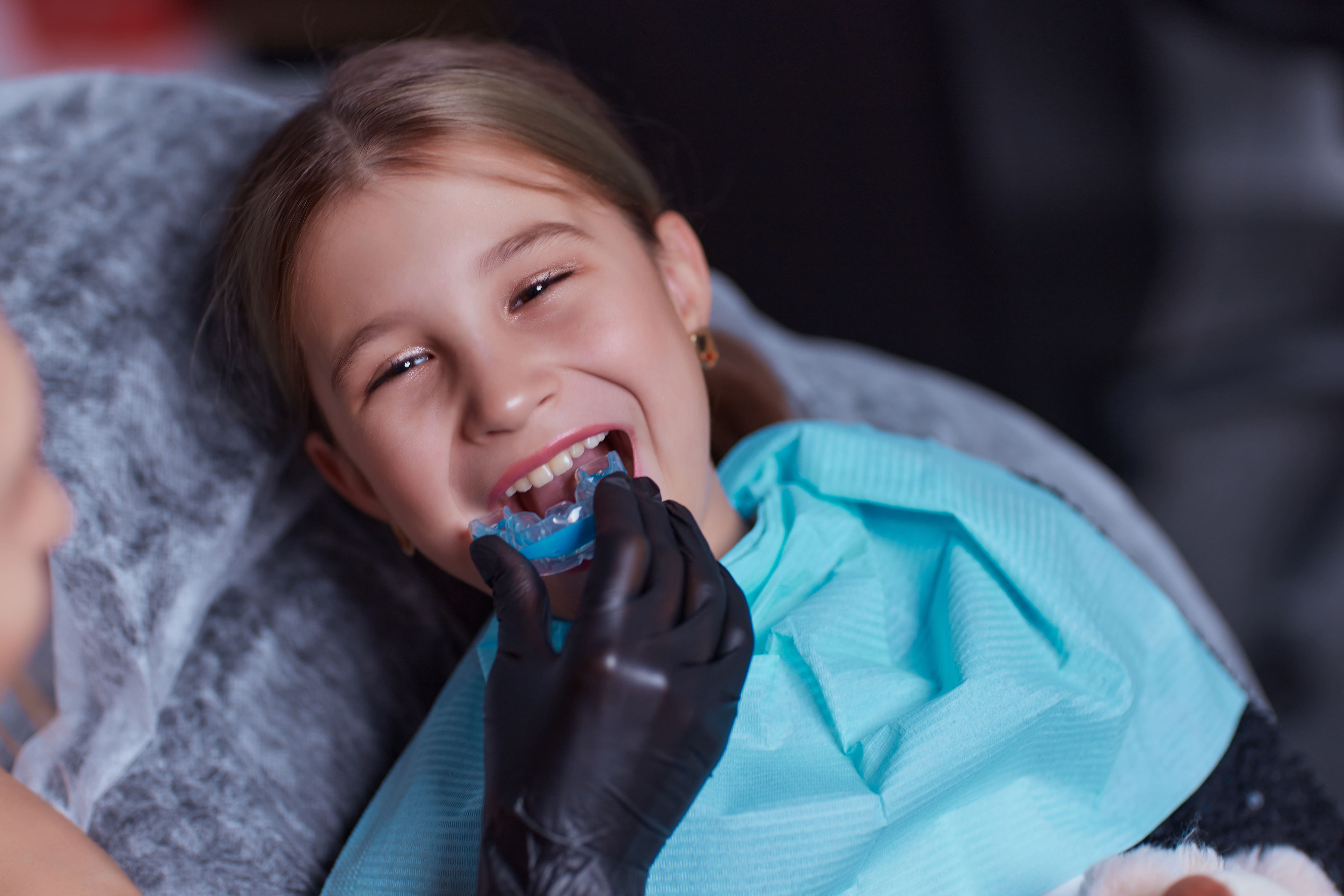 Young girl smiling while a clinician fits a blue oral myofunctional trainer appliance