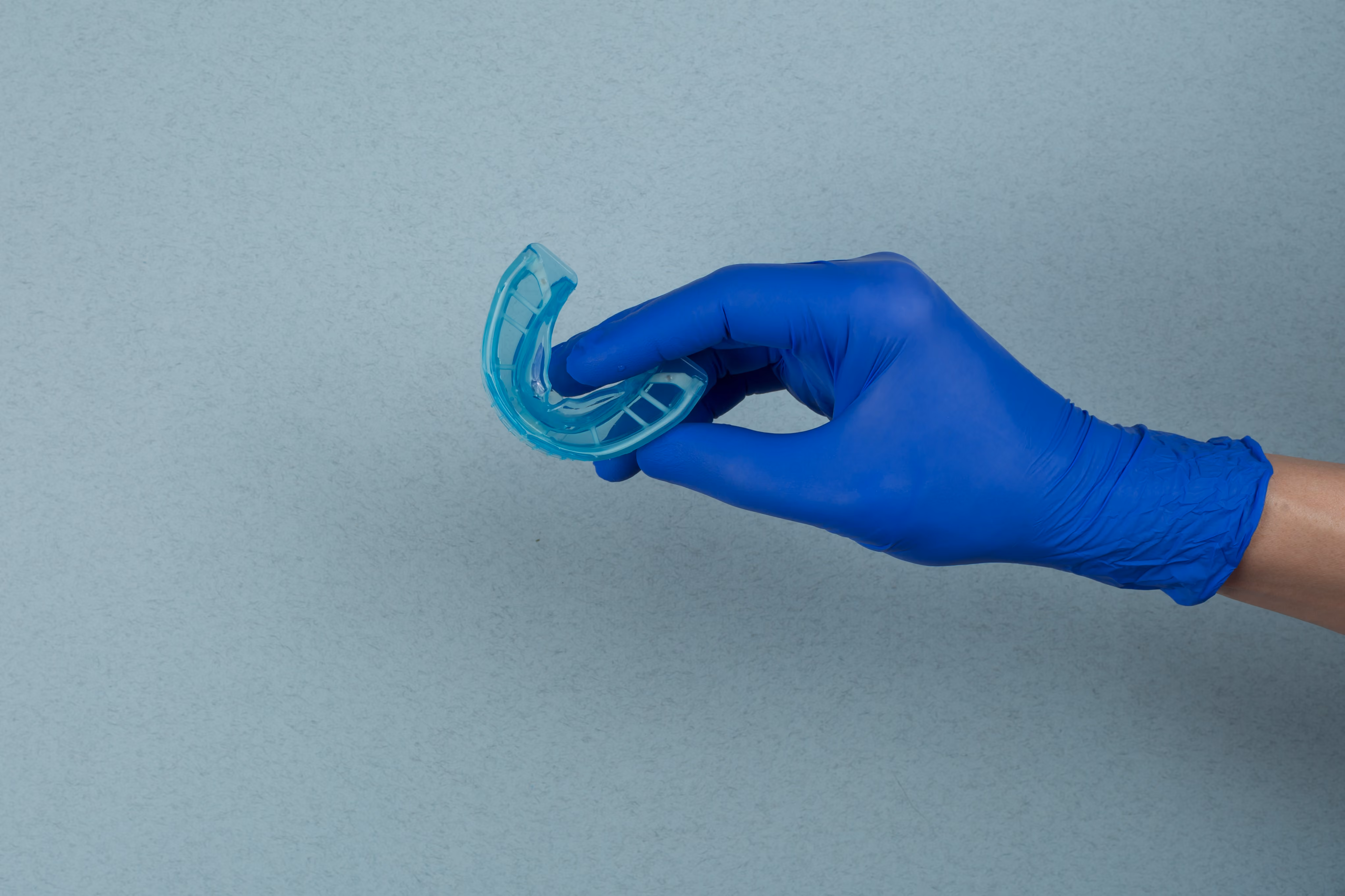 Gloved hand holding a clear oral appliance used in myofunctional therapy to retrain tongue and jaw posture