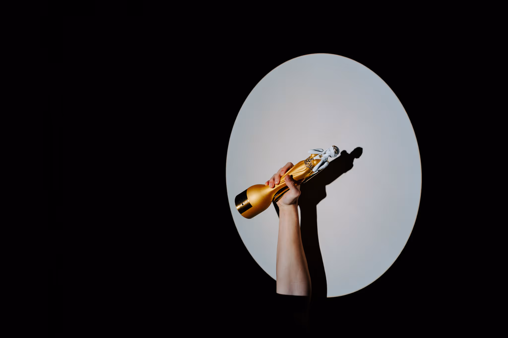 Krupni plan ruke koja pobjednički diže zlatni kipić New York Muse Awards ispred osvijetljenog kruga, potvrđujući status Gold Winnera.