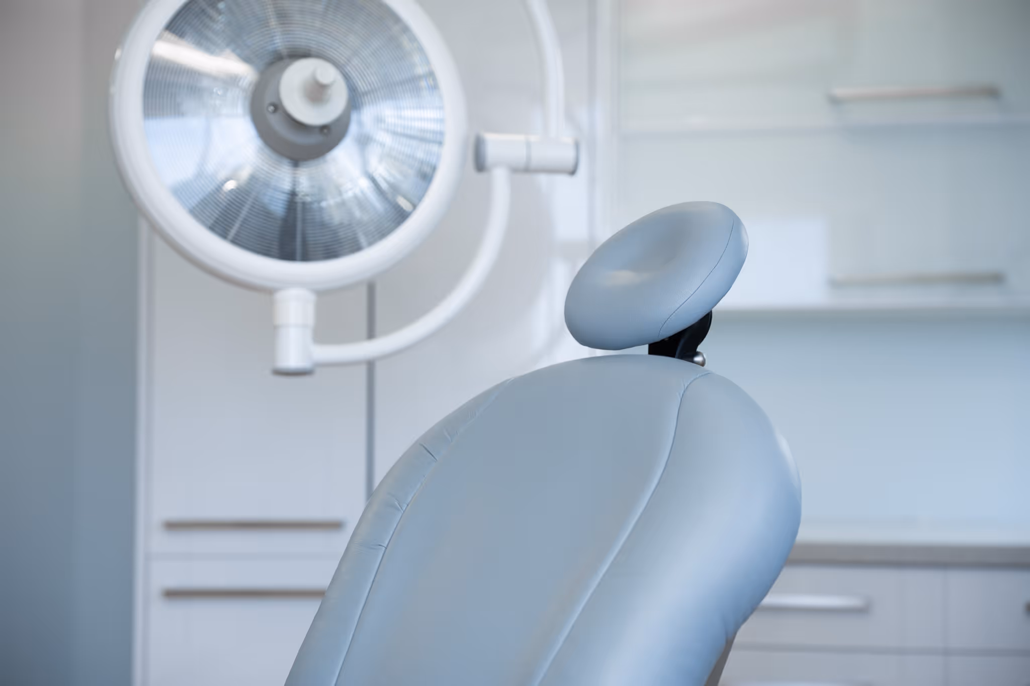 Close-up of a light blue dental chair with a round overhead lamp in a dental clinic.