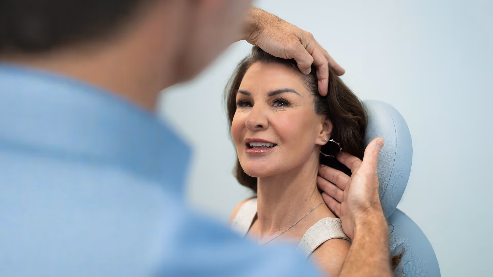 Woman smiling while a man adjusts her head and neck in a medical or consultation setting.
