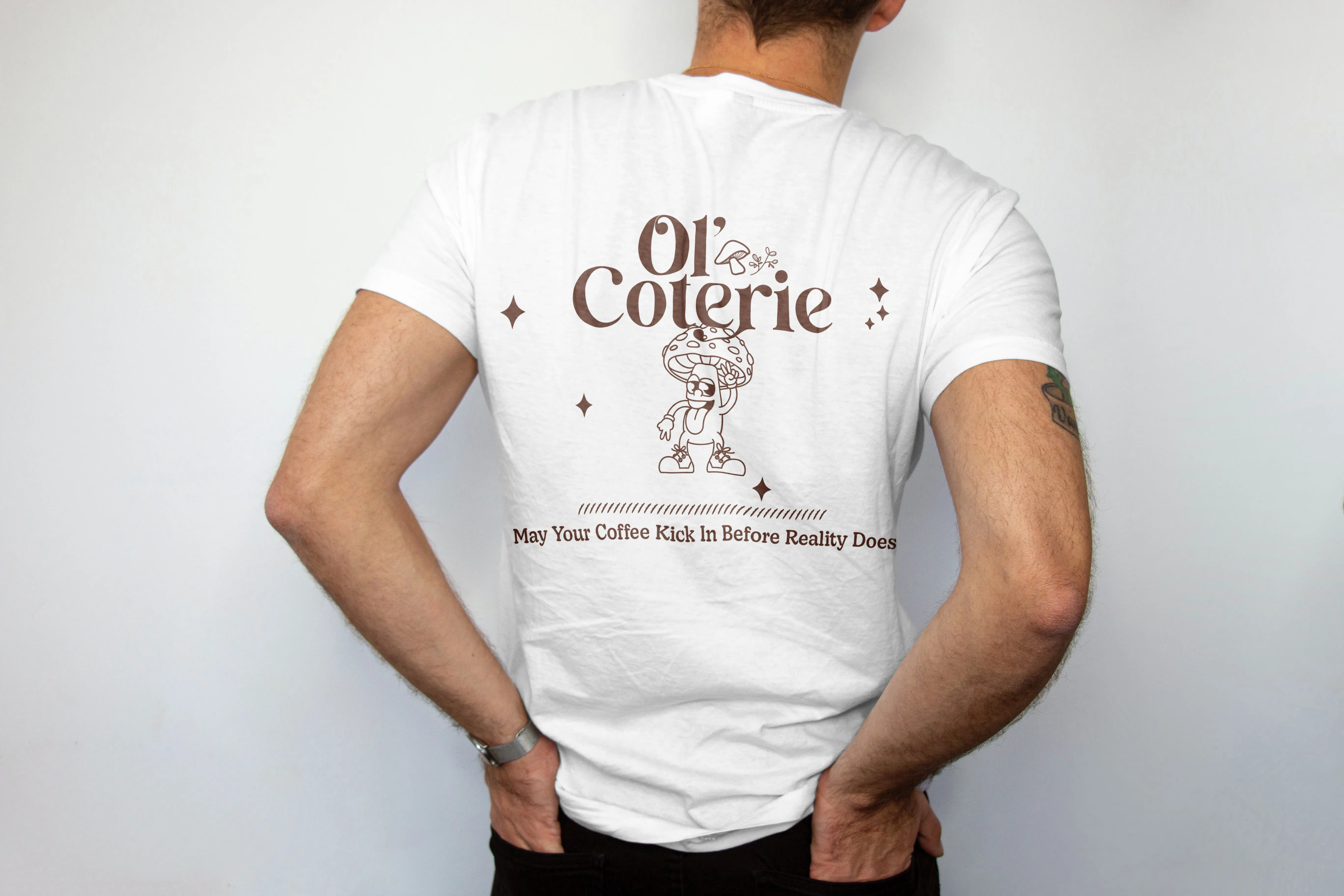 Back of white T-shirt with brown text 'Ol' Coterie' and a cartoon mushroom character, slogan below.