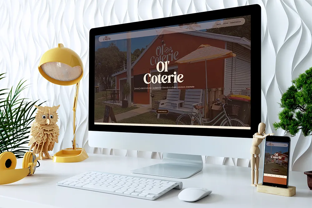 Modern desktop setup with a white keyboard, mouse, yellow lamp, owl figure, plant, and Ol' Coterie website displayed on screen and phone.