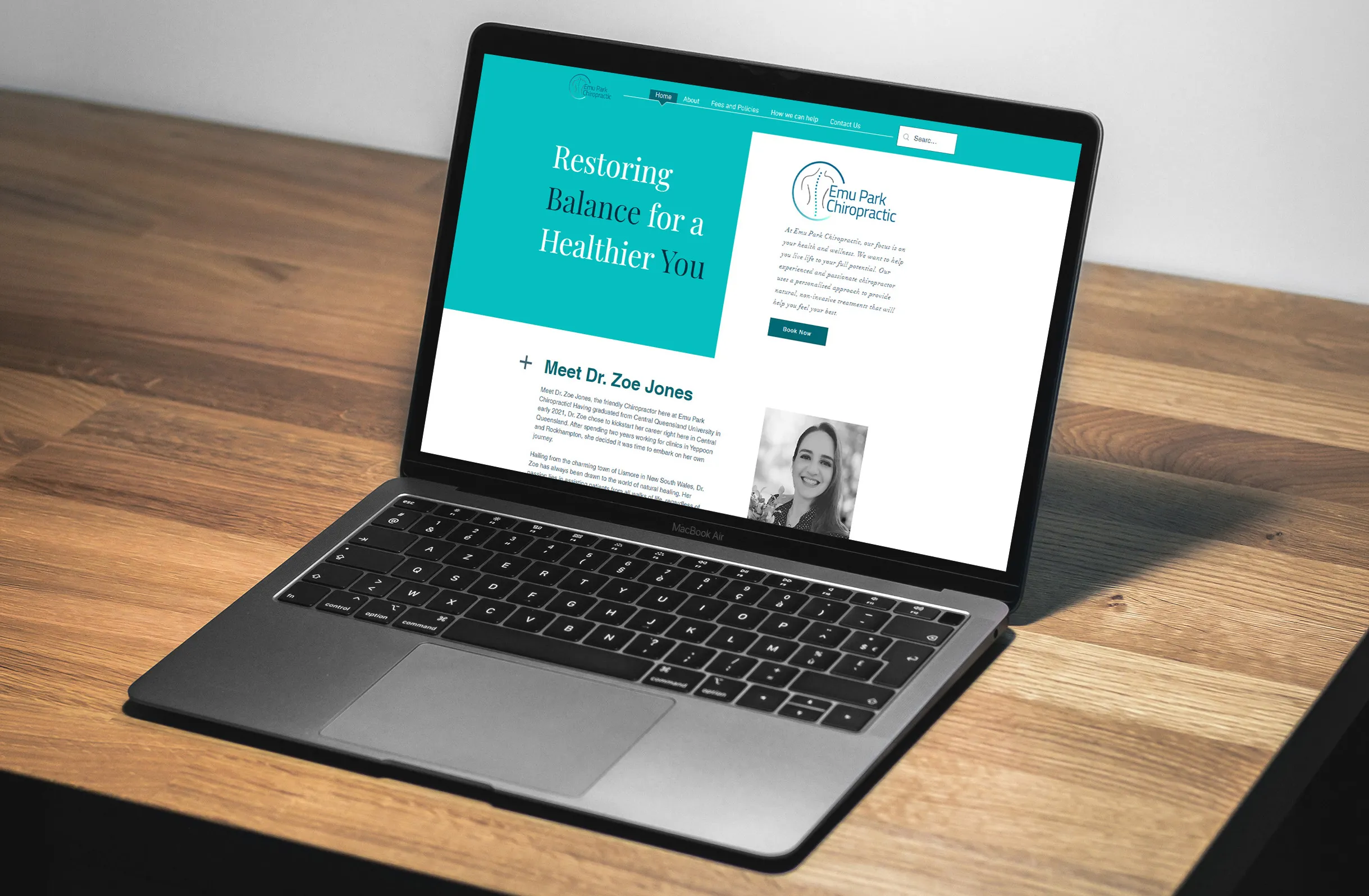 Open laptop on wooden table showing Emu Park Chiropractic website home page with teal and white design.