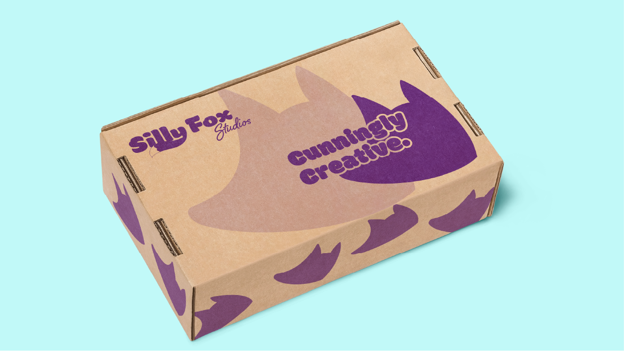 Rectangular brown cardboard box with purple fox head silhouettes and text reading 'Silly Fox Studios' and 'Cunningly Creative' on a light blue background.