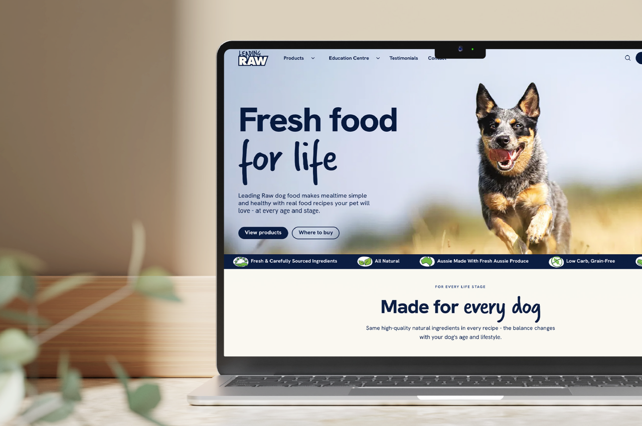 Laptop on a wooden surface displaying a dog food website with a happy running dog on the screen and text saying Fresh food for life and Made for every dog.
