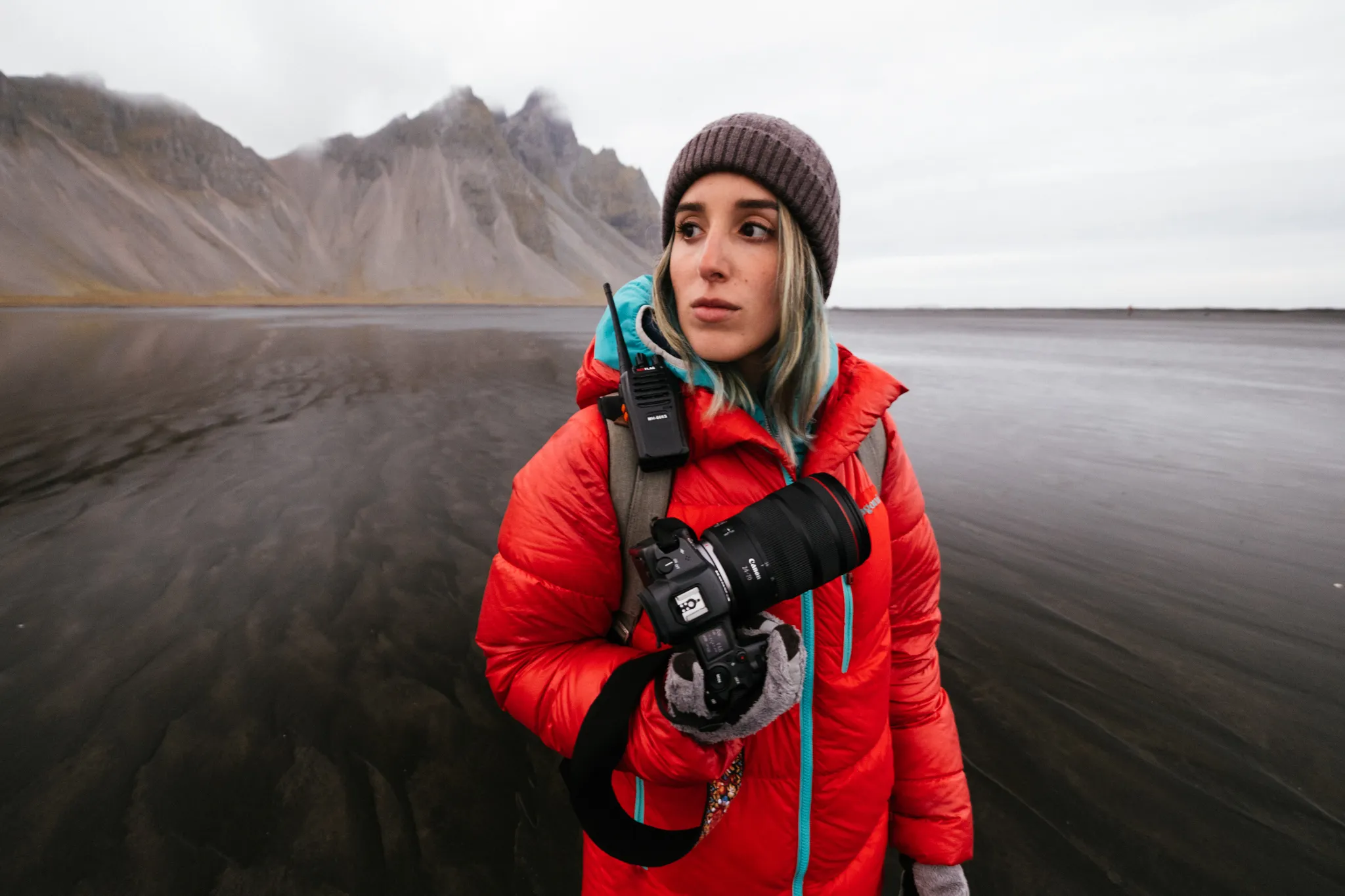 Documentary wedding photographer in red winter jacket holding a Canon camera on an Icelandic black sand beach