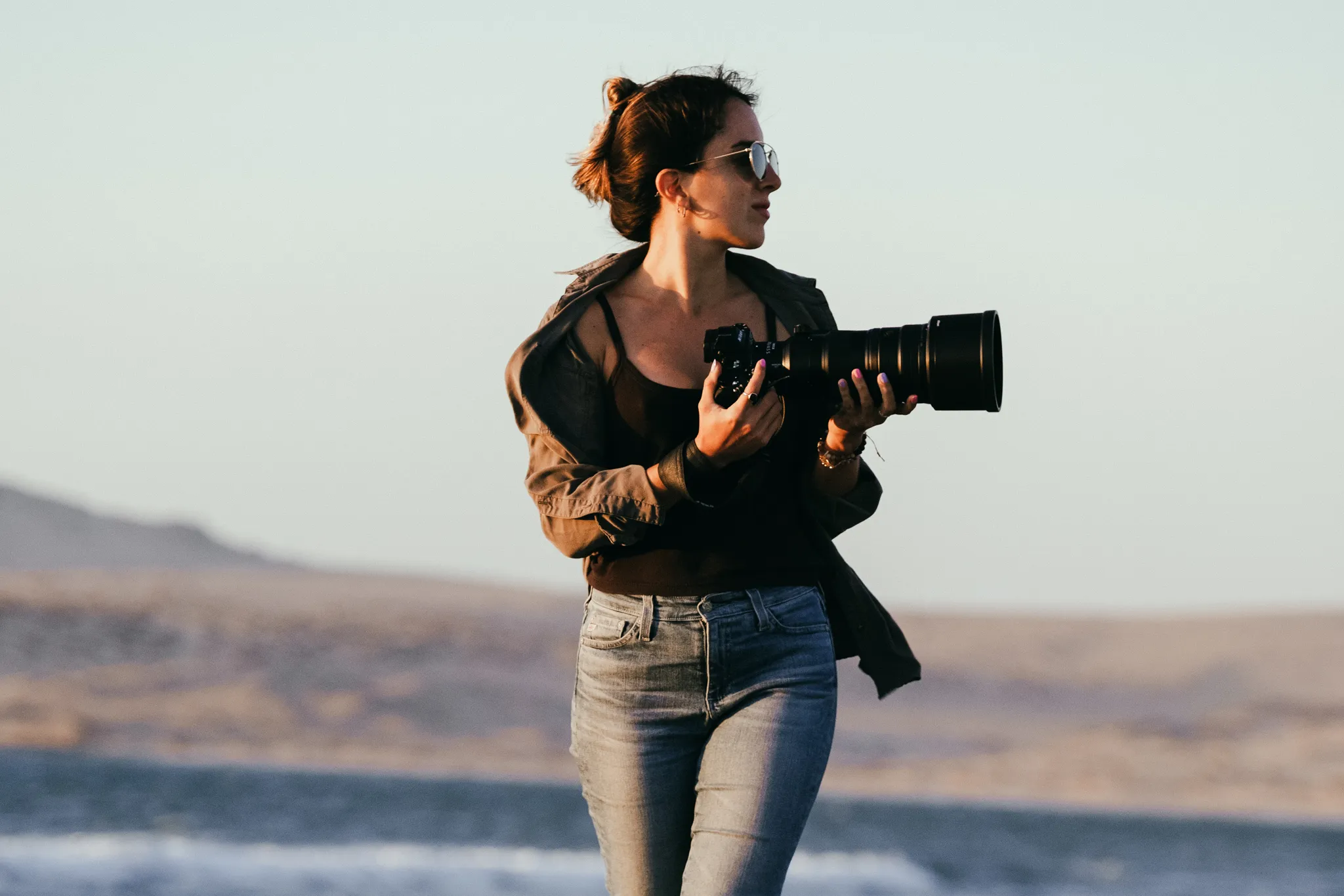 Documentary wedding photographer woman holding a professional camera with telephoto lens during a golden hour outdoor shoot