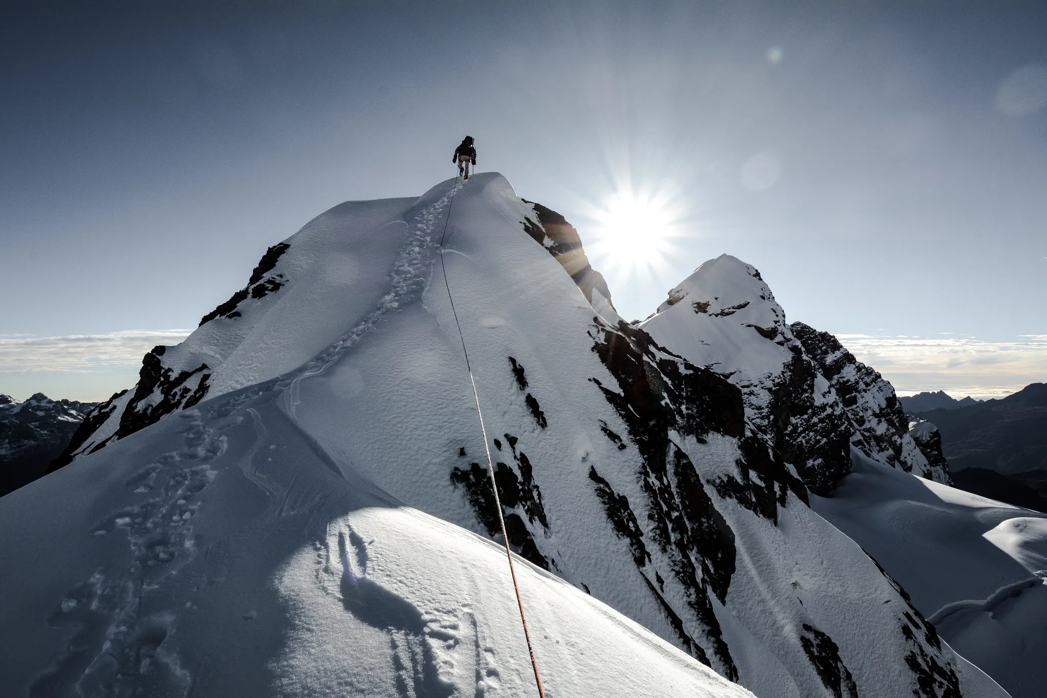 Documentary wedding photographer adventure elopement image of a mountaineer reaching a snowy alpine summit at sunrise with rope