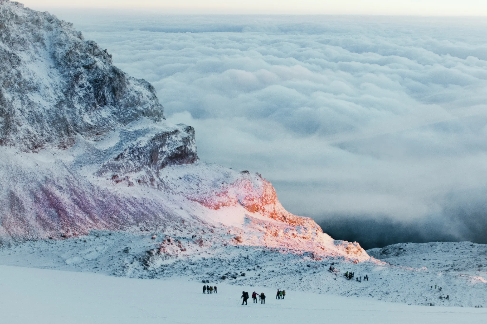Documentary wedding photographer captures trekkers crossing a vast snow-covered glacier above the clouds at sunrise