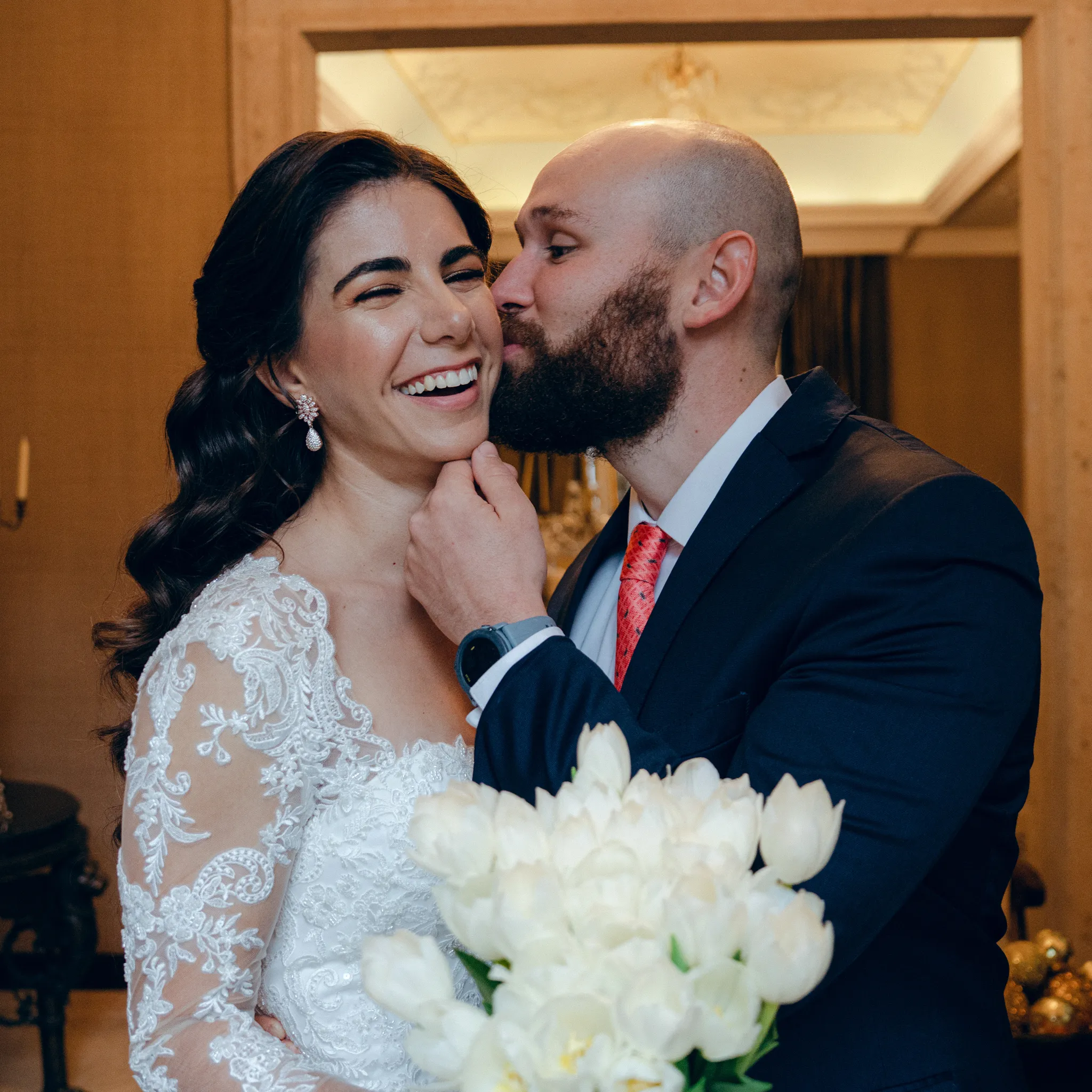 Bride laughing as groom kisses her cheek during wedding celebration