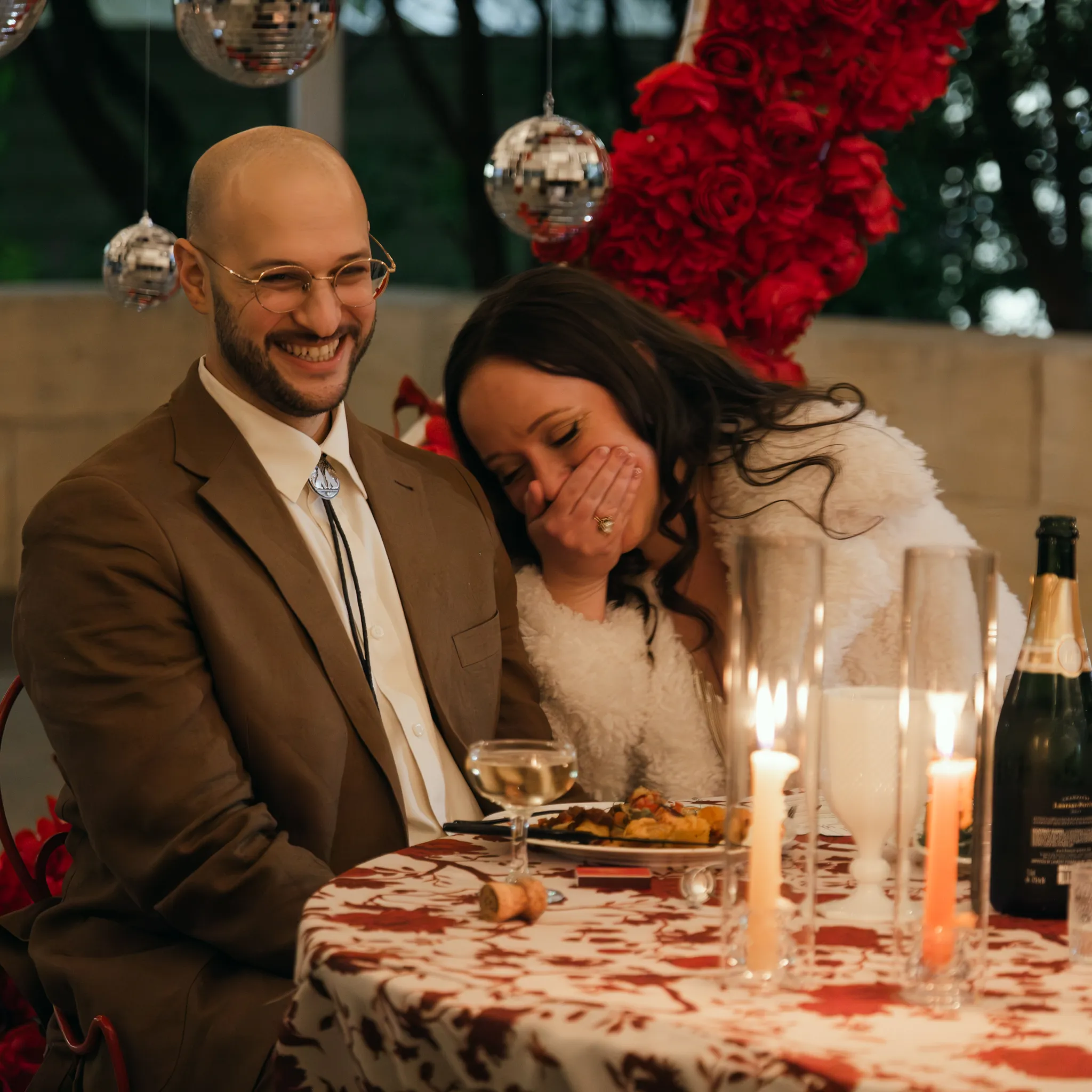 Documentary wedding photographer couple laughing together at a candlelit wedding reception with disco balls and red roses