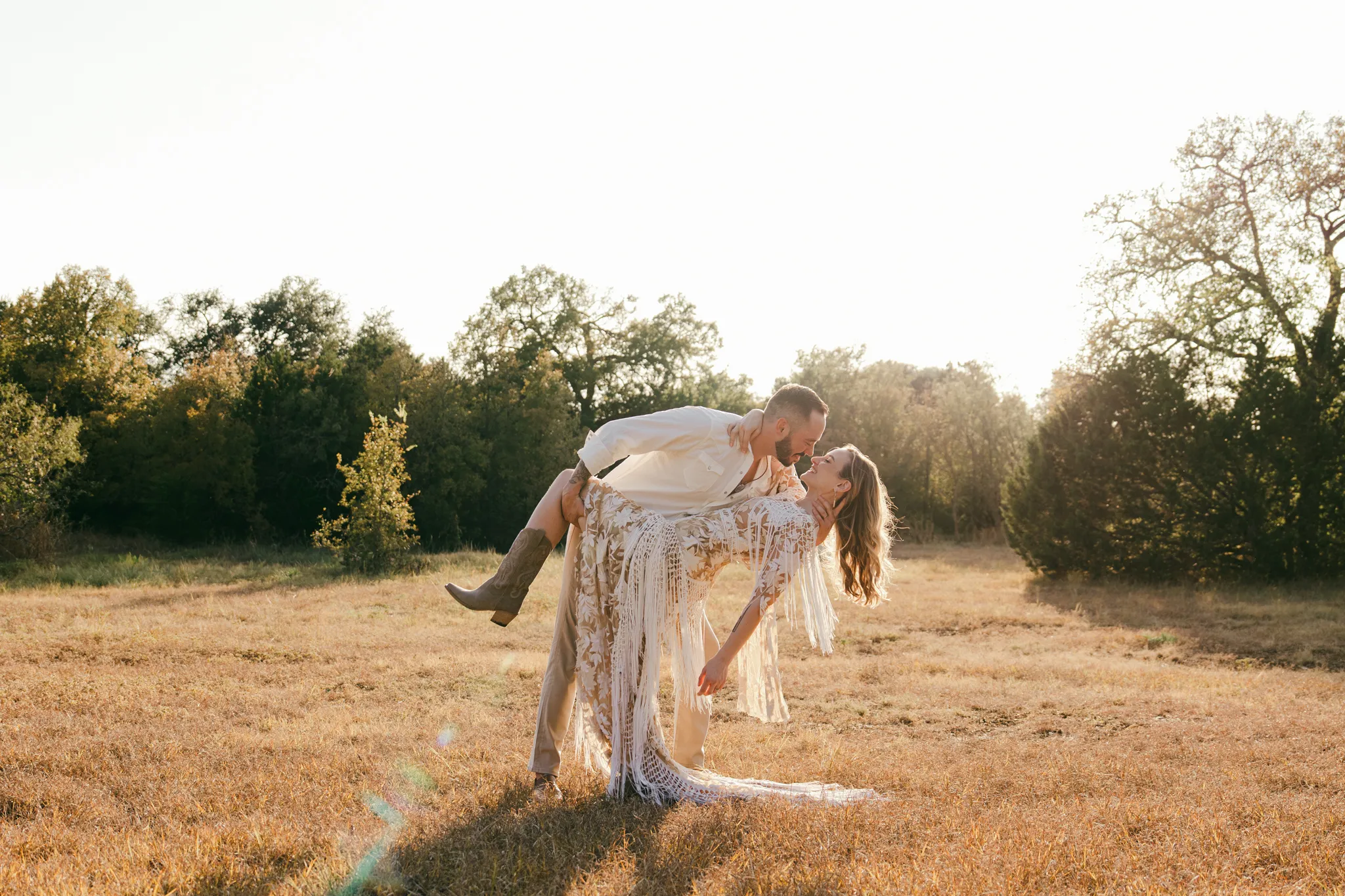Austin Texas wedding photographer captures groom lifting bride in a bohemian fringe dress at golden hour in a Hill Country field