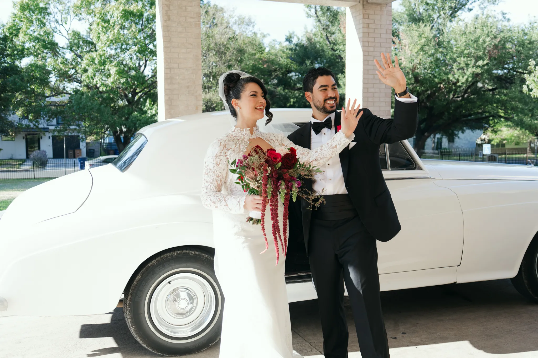 Austin Texas wedding photographer joyful bride and groom waving next to a vintage white car holding a red bouquet