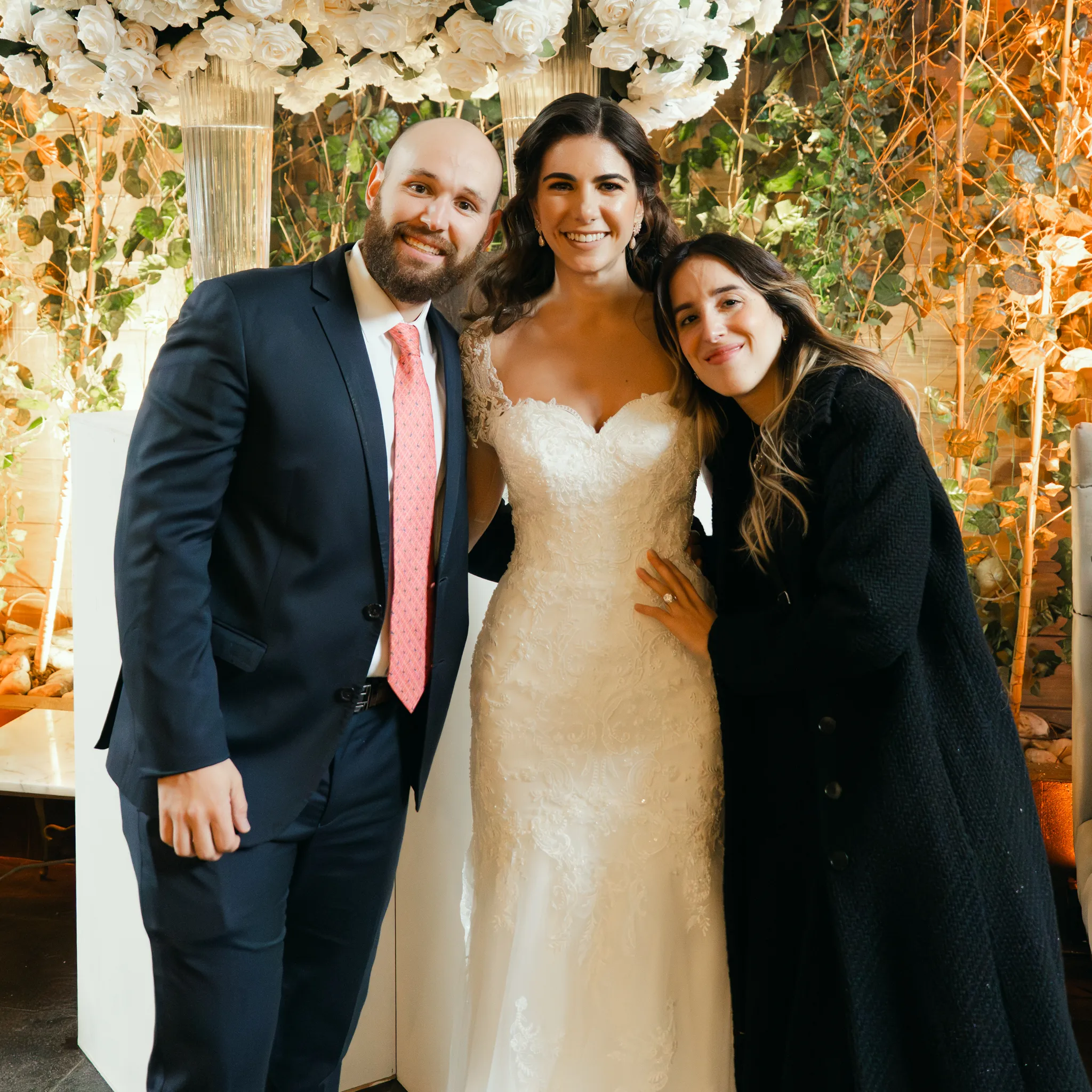 Marcela Briere Austin Texas wedding photographer posing with bride and groom in front of a white floral wedding backdrop