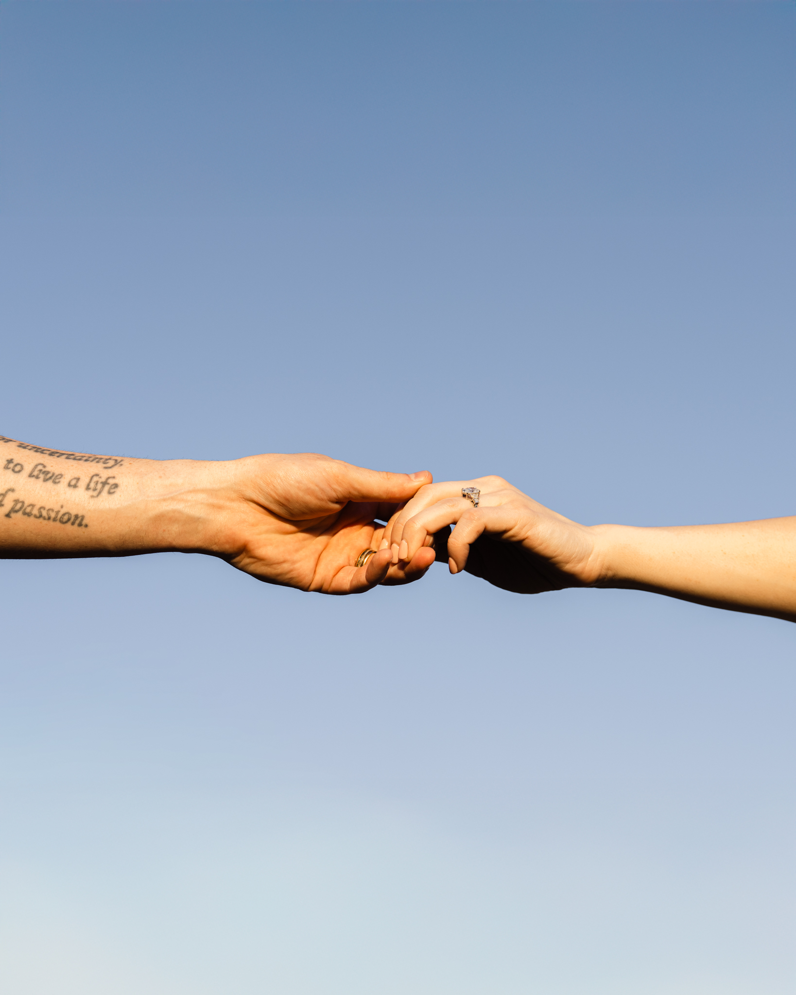Austin Texas wedding photographer close-up of couple holding hands against a blue sky with tattoo and engagement ring