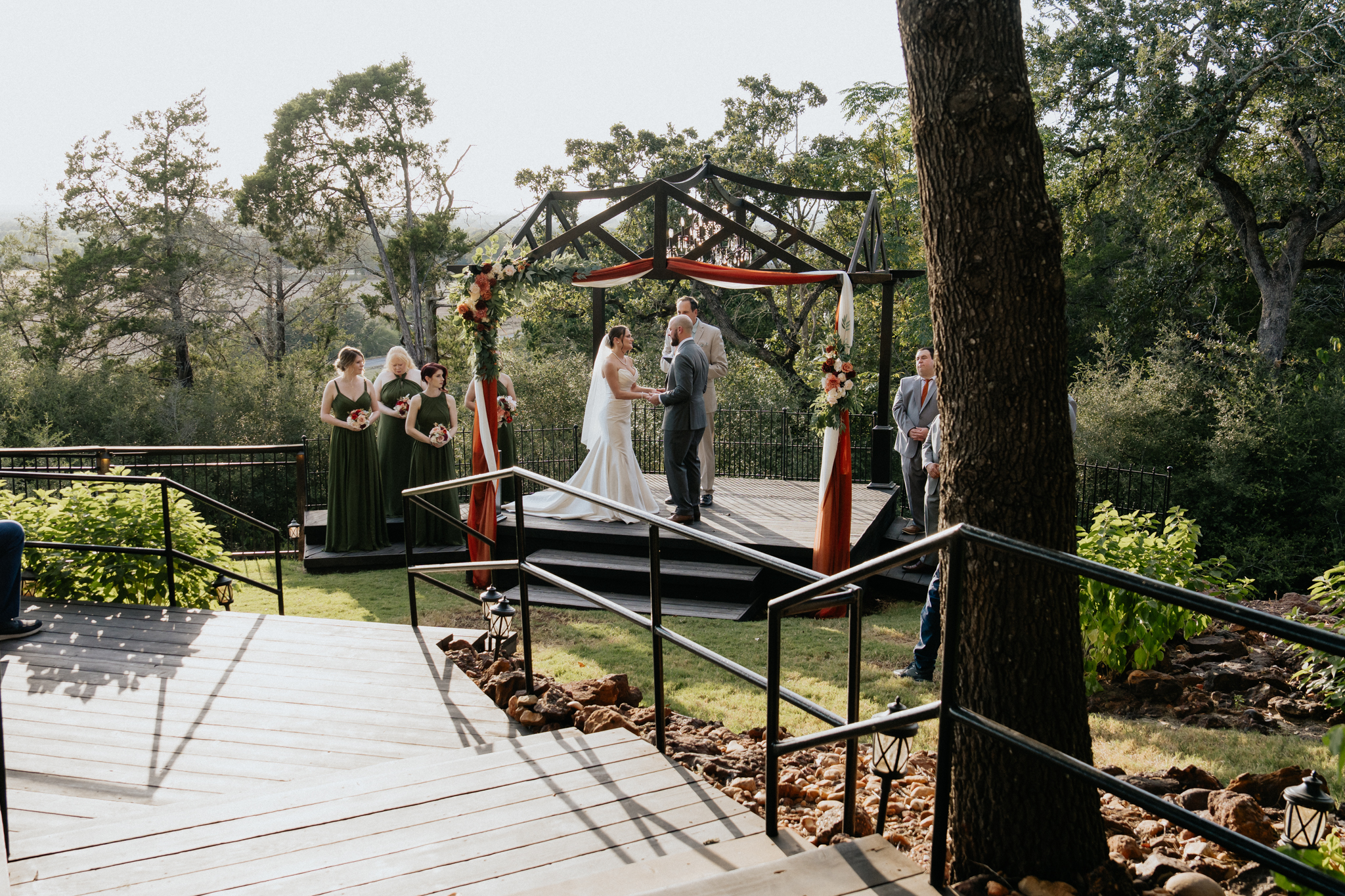 Outdoor wedding ceremony with bride, groom, and wedding party surrounded by trees, photographed by Austin Texas wedding photographer Moments By Marcela