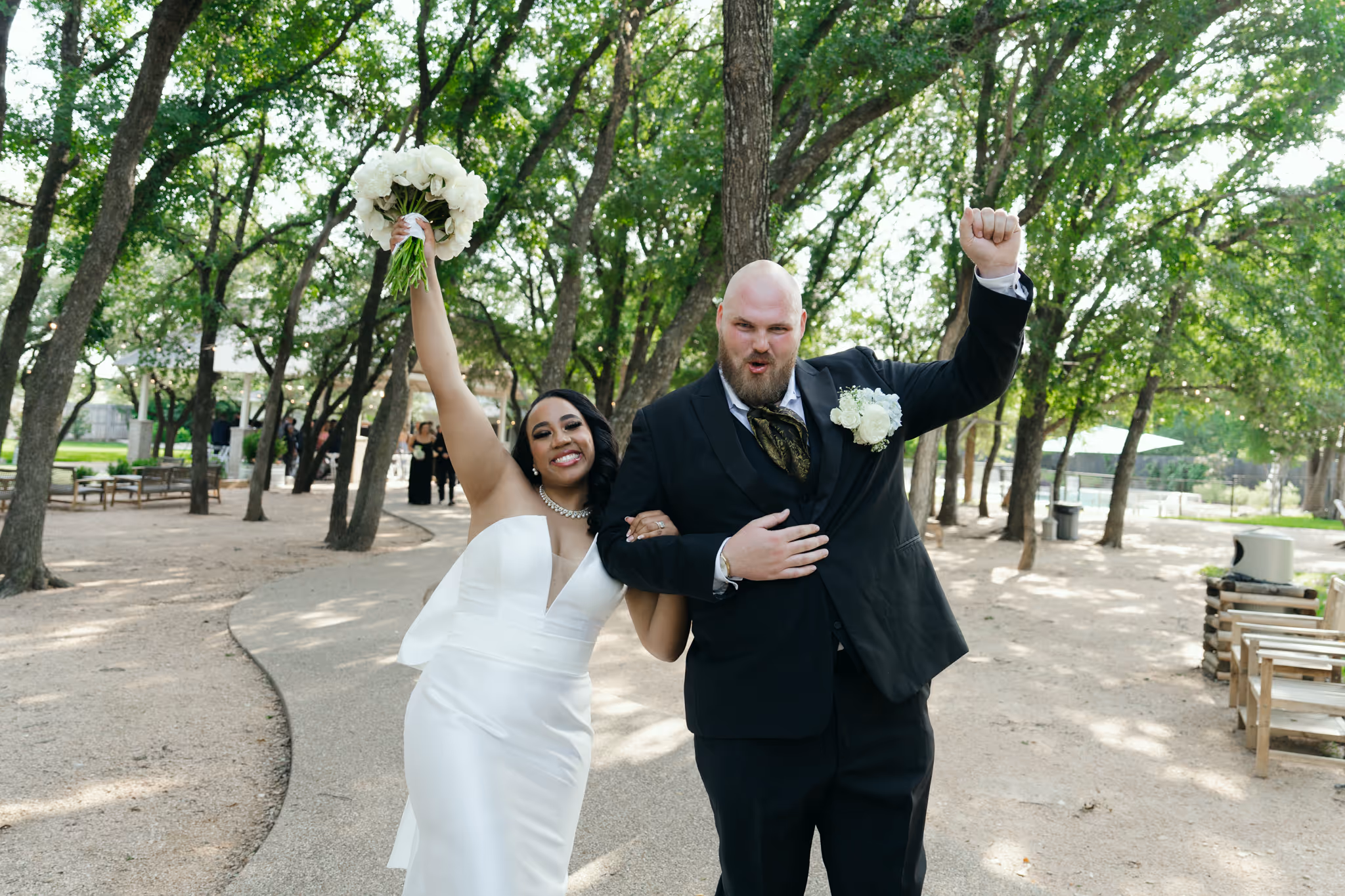 Bride and groom celebrating after their ceremony, arms raised in joy surrounded by oak trees.