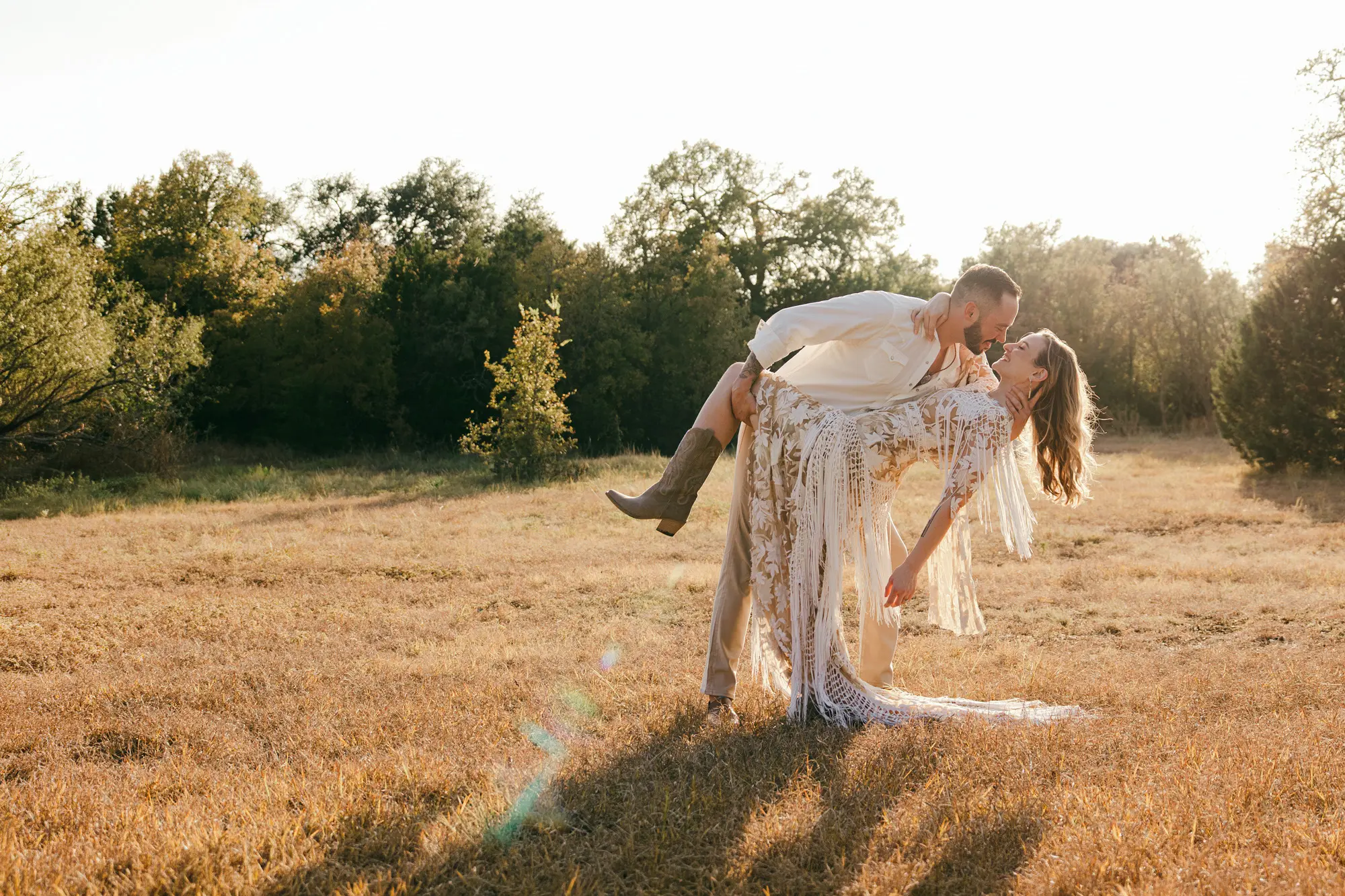 Austin Texas wedding photographer captures groom lifting bride in a bohemian fringe dress at golden hour in a Hill Country field