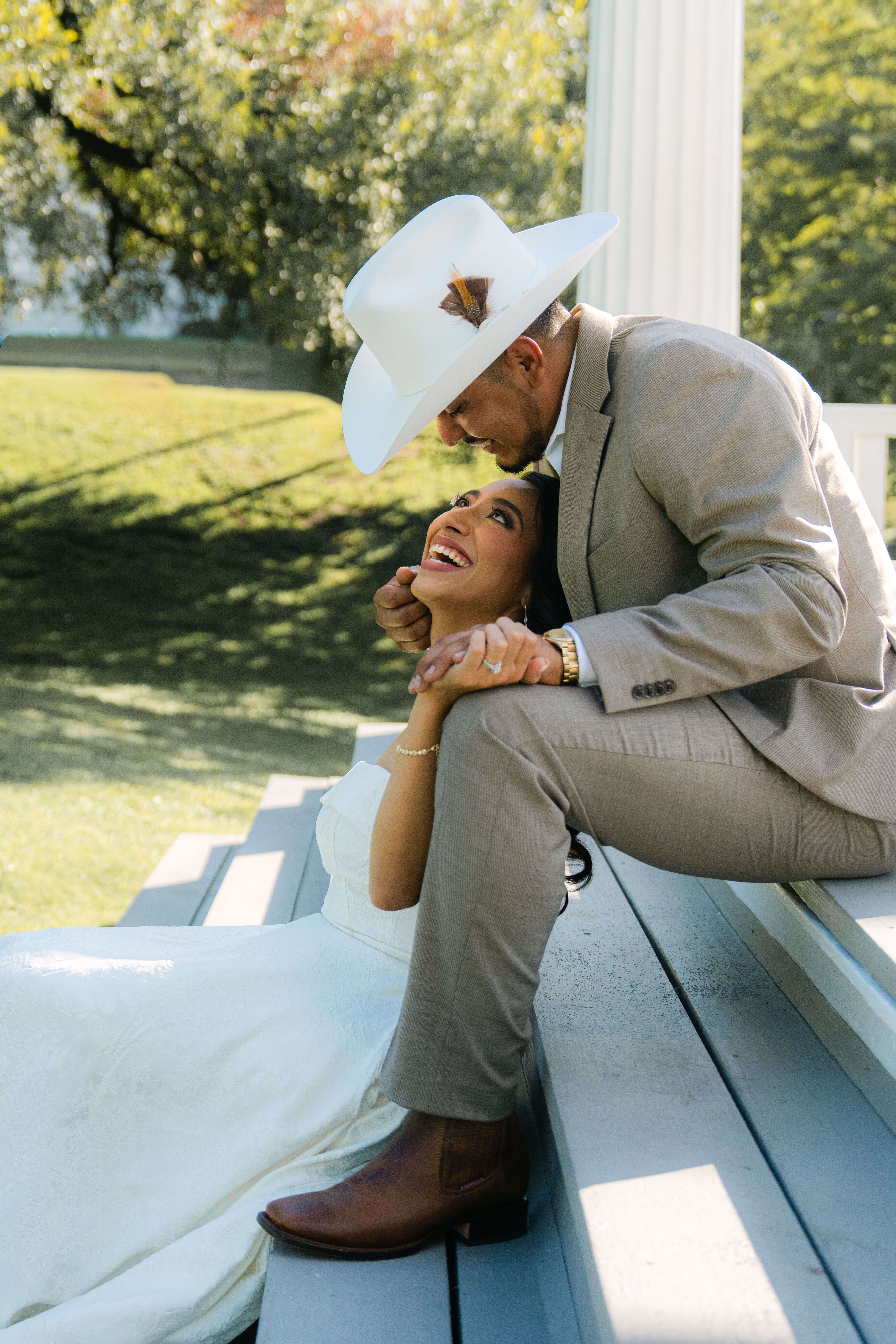 Bride laughing while groom in white cowboy hat holds her close on the gazebo steps near the Travis County Courthouse