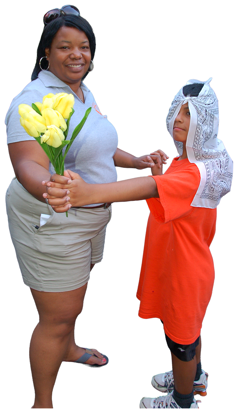 Ms Donna smiling holding yellow tulips while a camper wearing an orange shirt and a white bandana on his head holds her hands.