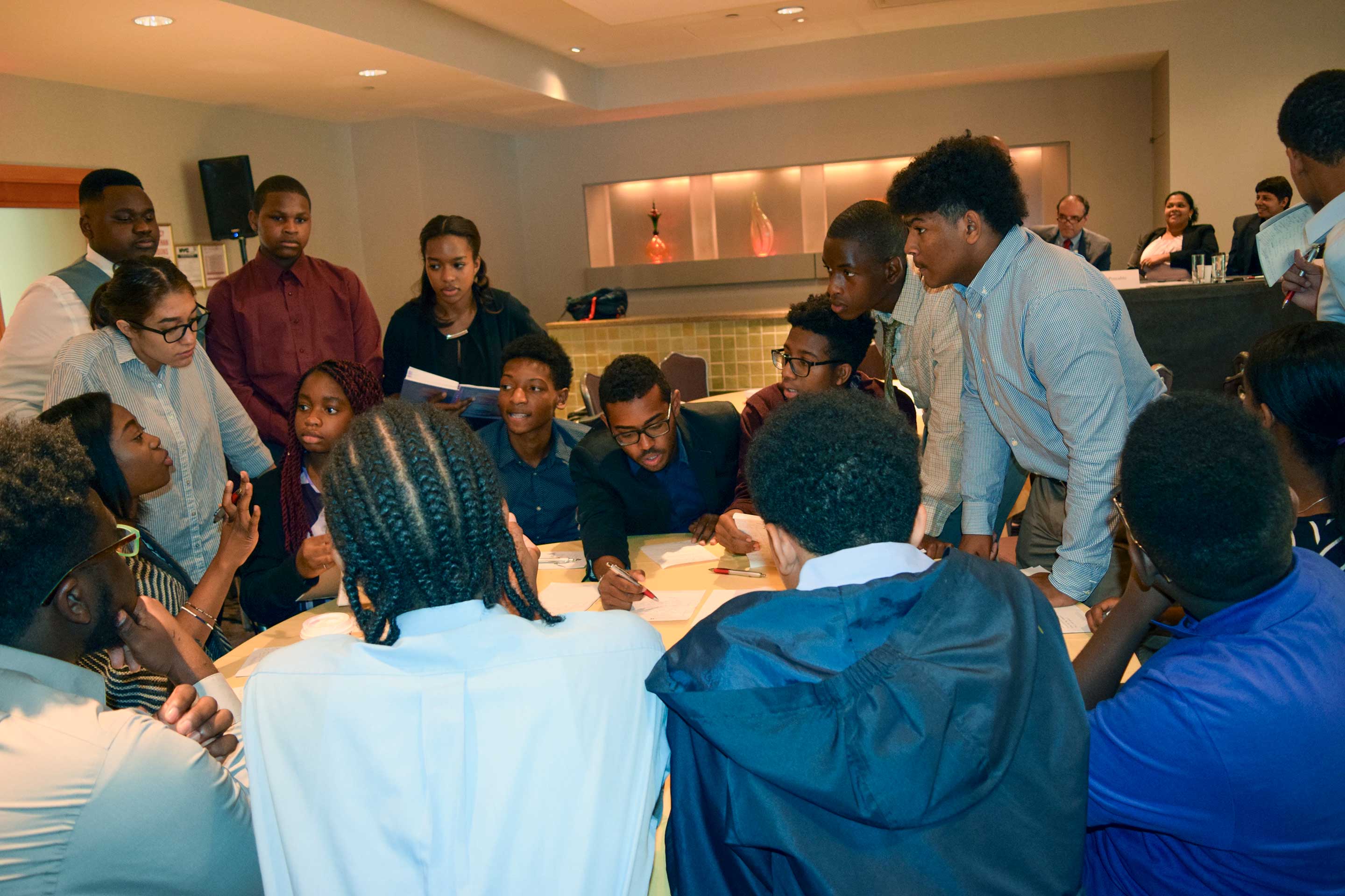 A group of young people engaged in a collaborative discussion around a table in a conference room during Student Adventures in Leadership (SAIL)