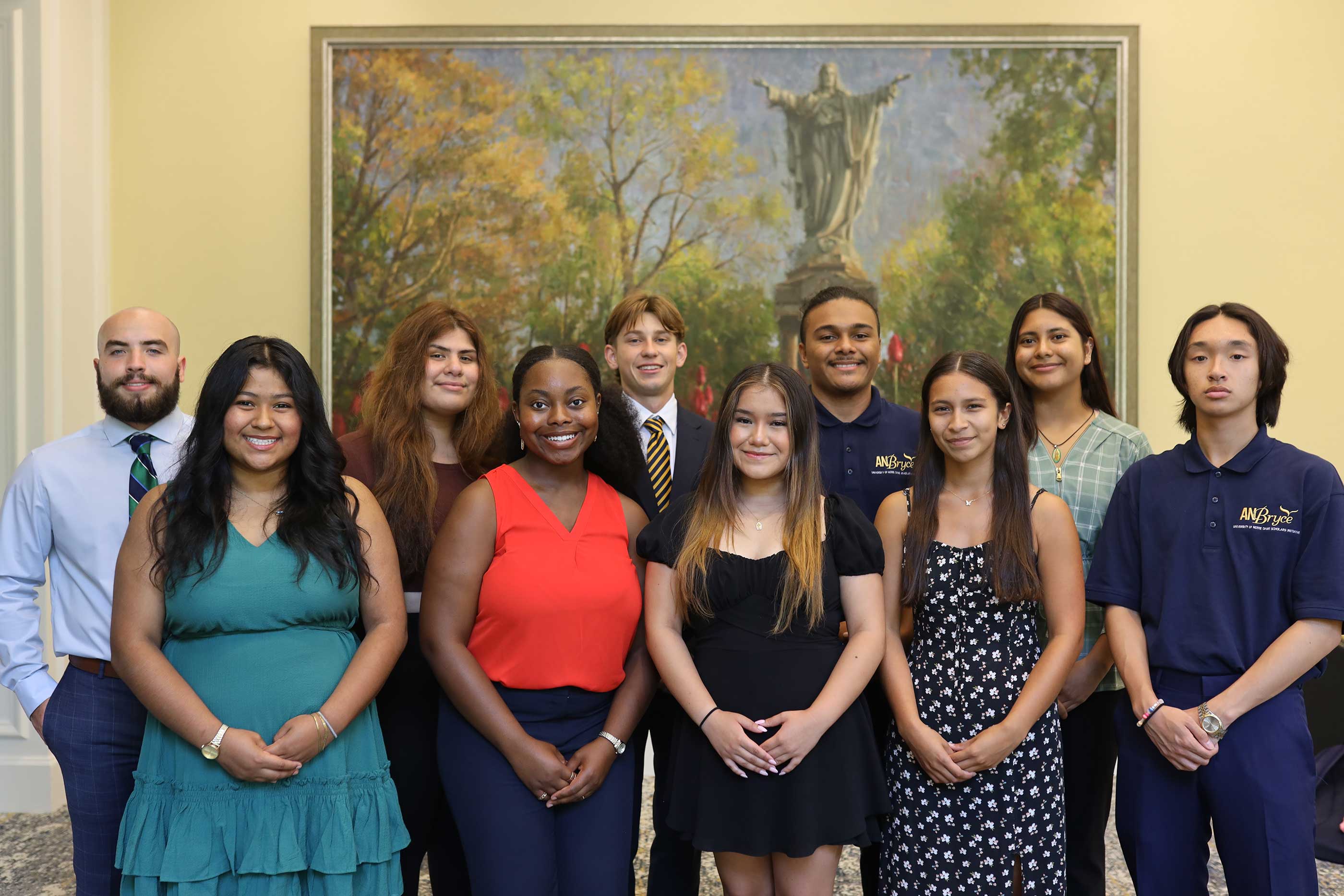 Group of ten diverse young adults in the AnBryce Scholors program standing indoors in front of a framed painting of a statue and trees, smiling and posing for a photo
