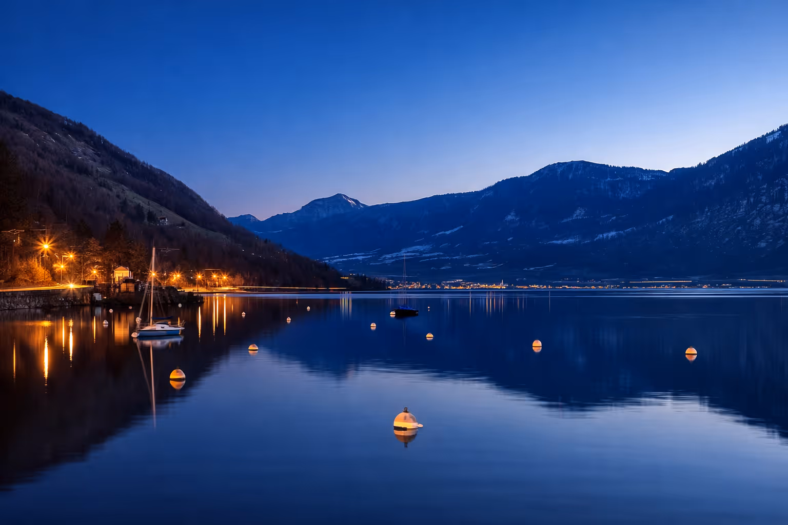 Atmospheric nighttime photography of a Swiss lake with lights reflecting on the water, symbolizing the company's "Made in Switzerland" quality.