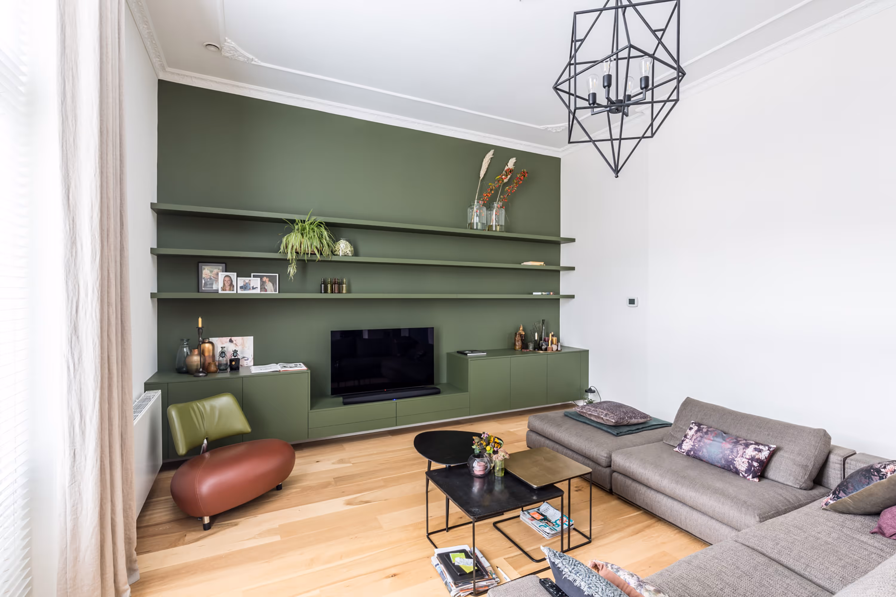 Moderne woonkamer met groene ingebouwde wandplanken, televisie, grijze hoekbank en houten vloer.