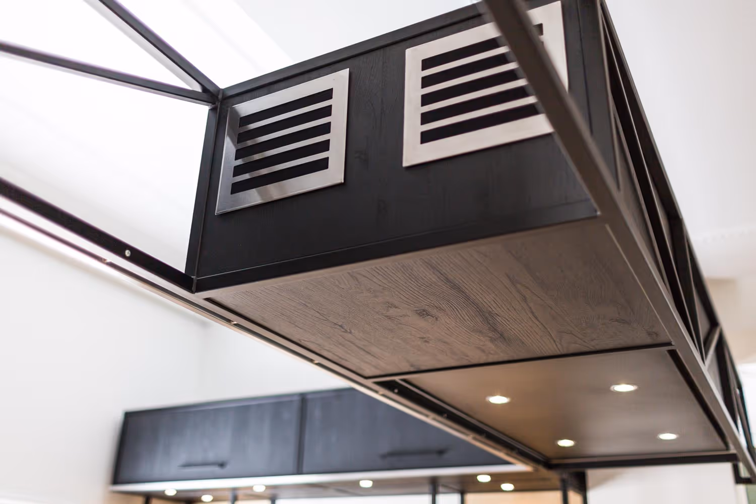 Close-up van een moderne afzuigkap met zwart hout en metalen ventilatiepanelen, met ingebouwde verlichting aan de onderzijde.