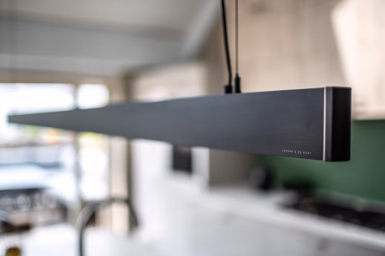 Moderne zwarte rechthoekige hanglamp boven een keukenruimte met onscherpe achtergrond.