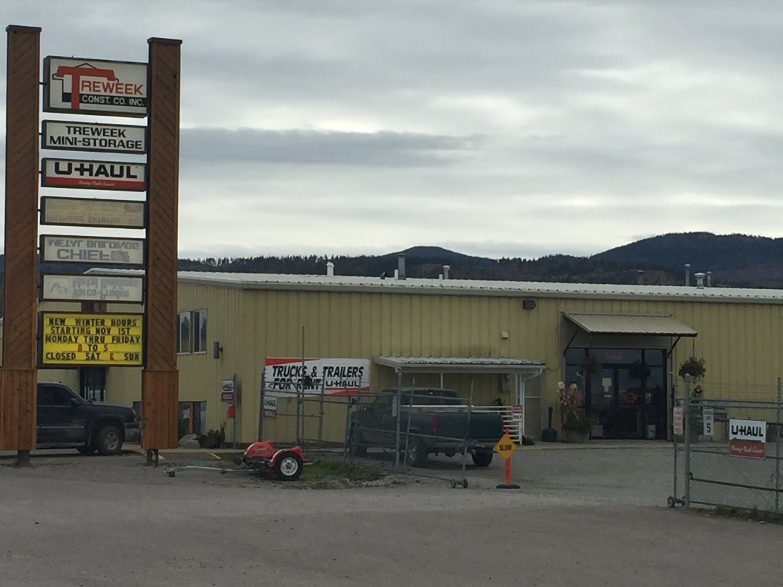 Exterior view of Treweek Mini-Storage with a large sign, a yellow building, parked trucks, and the U-Haul logo visible.