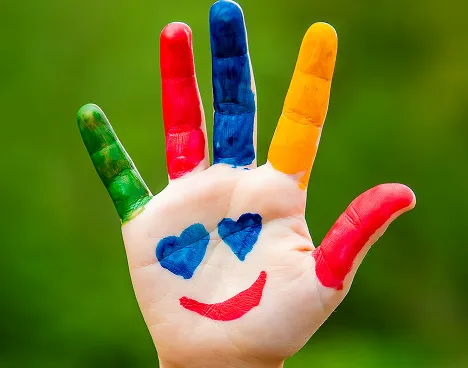 Hand with fingers painted in green, red, blue, yellow, and red, with two blue hearts and a red smile drawn on the palm.