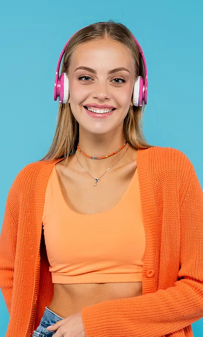 Smiling young woman wearing pink headphones, an orange crop top, and a matching orange cardigan against a blue background.