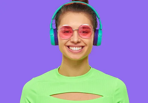 Smiling young woman wearing large teal headphones, pink sunglasses, and a neon green top against a purple background.