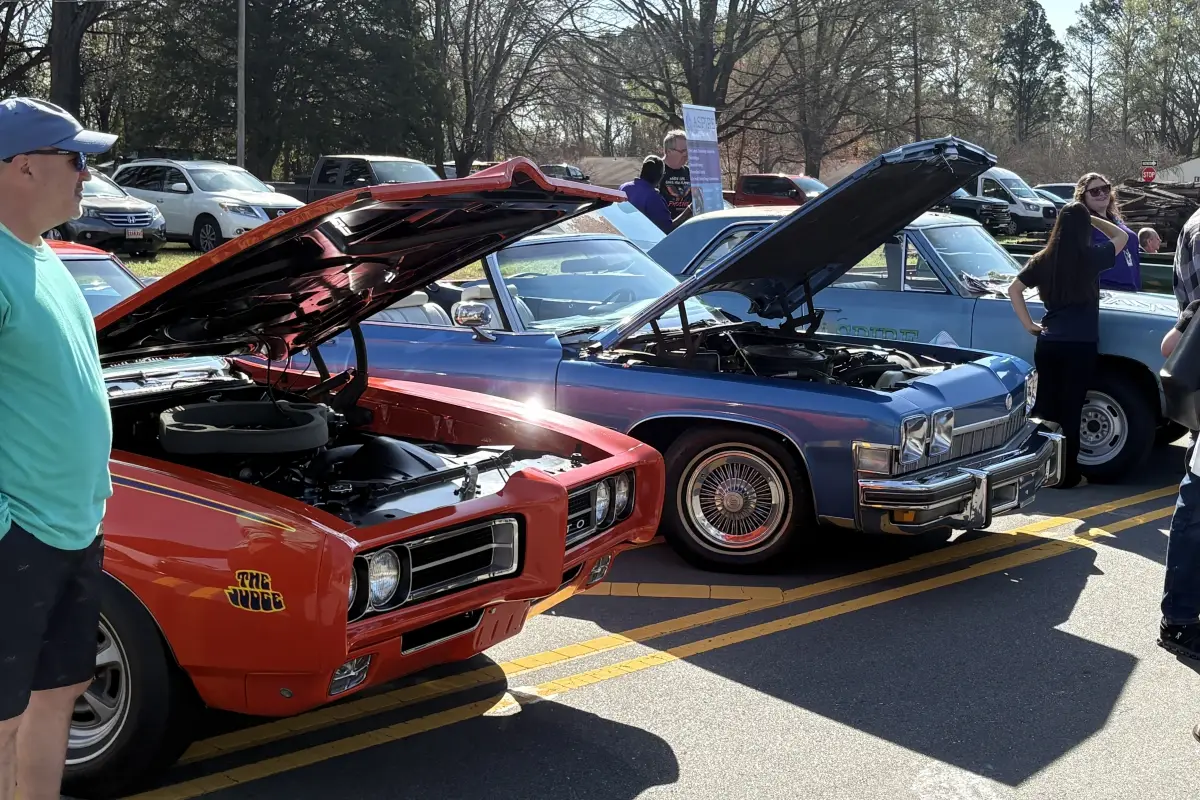 Three adults exercising in a modern gym, holding dumbbells in a high plank position while performing renegade rows; the person in front pulls a dumbbell upward as the others mirror the movement behind them.