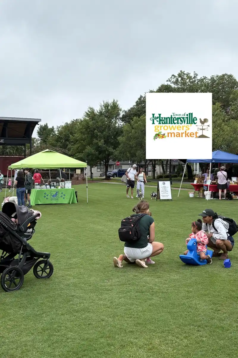 Families browsing vendor tents at the Huntersville Growers' Market, Huntersville's weekly farmers market in Veterans Park