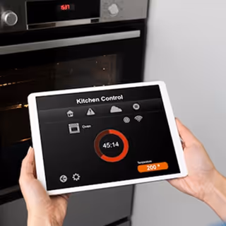 Person holding a tablet displaying a kitchen control interface with oven timer and temperature settings.