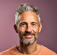 Smiling middle-aged man with gray hair and beard wearing a peach-colored shirt against a purple background.
