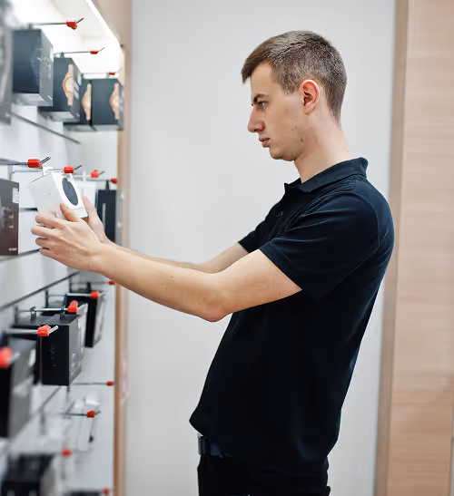 Man in black shirt examining a boxed electronic device on a store display wall.